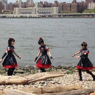 image id: a photo of babymetal playing on a stony river bank. they are wearing their first black and red stage outfits. end id.
